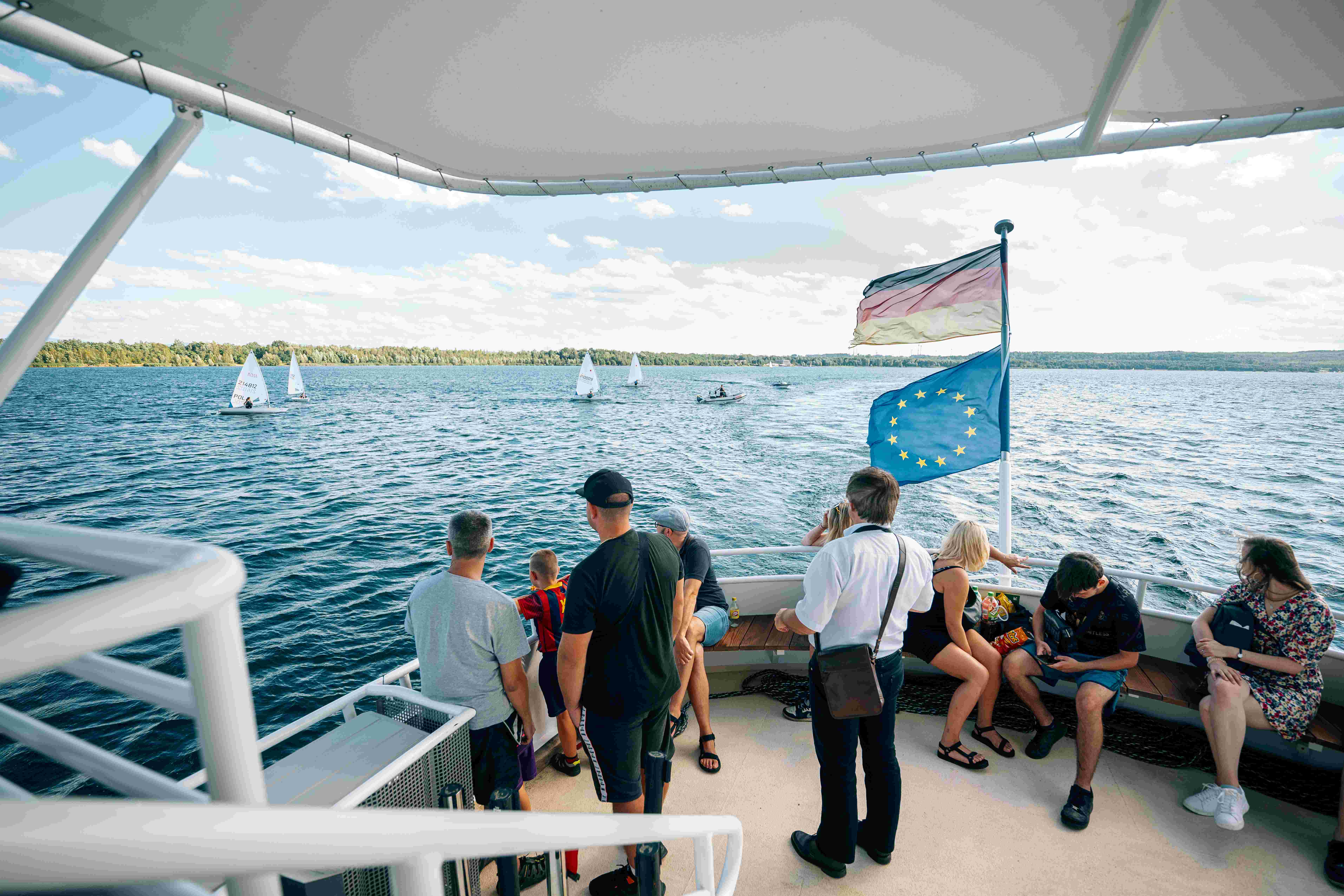 Cestující stojí na přídi lodi a dívají se na jezero.